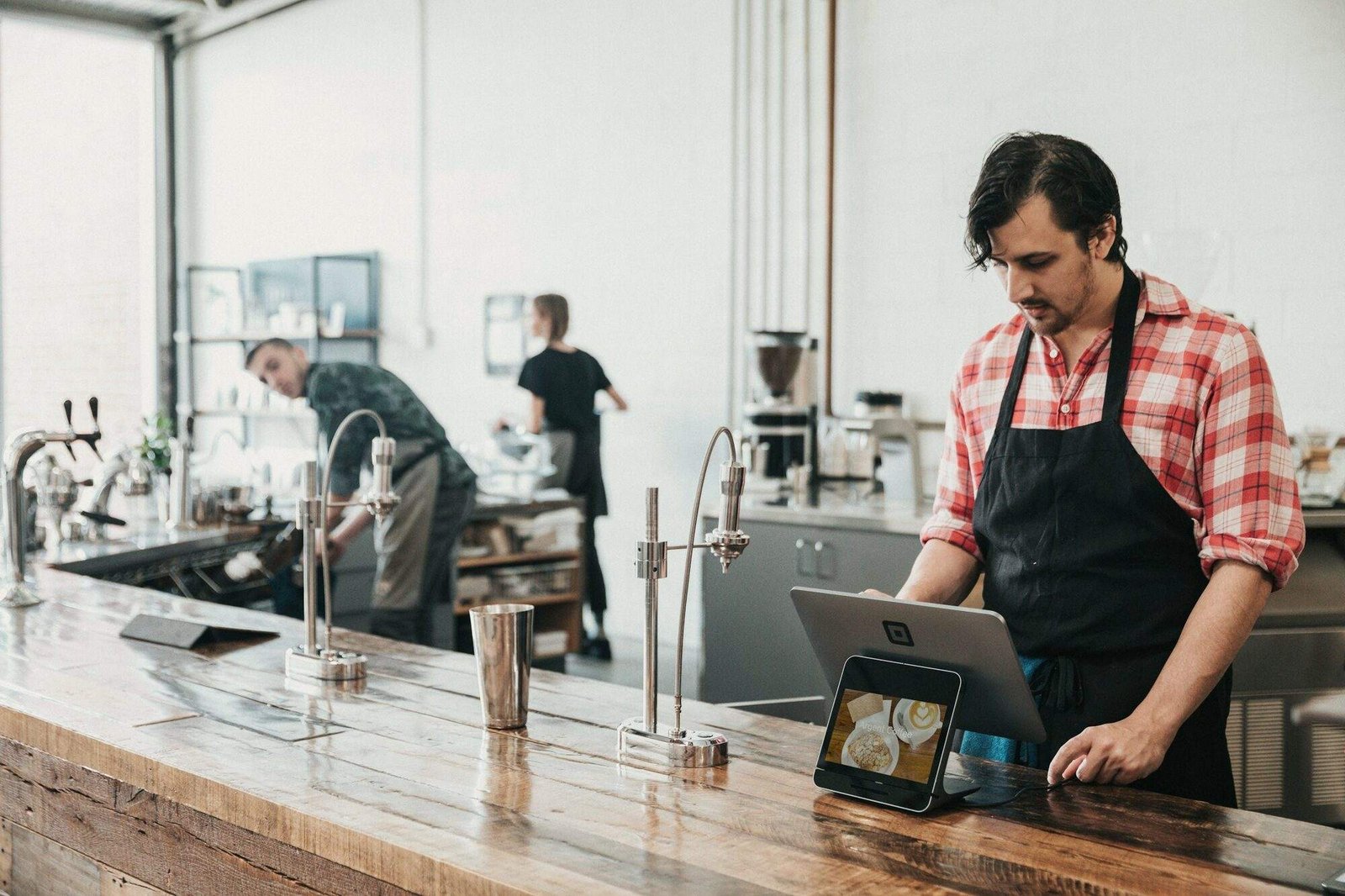 Encargado de una cafetería consultando reservas en una tableta junto a la barra